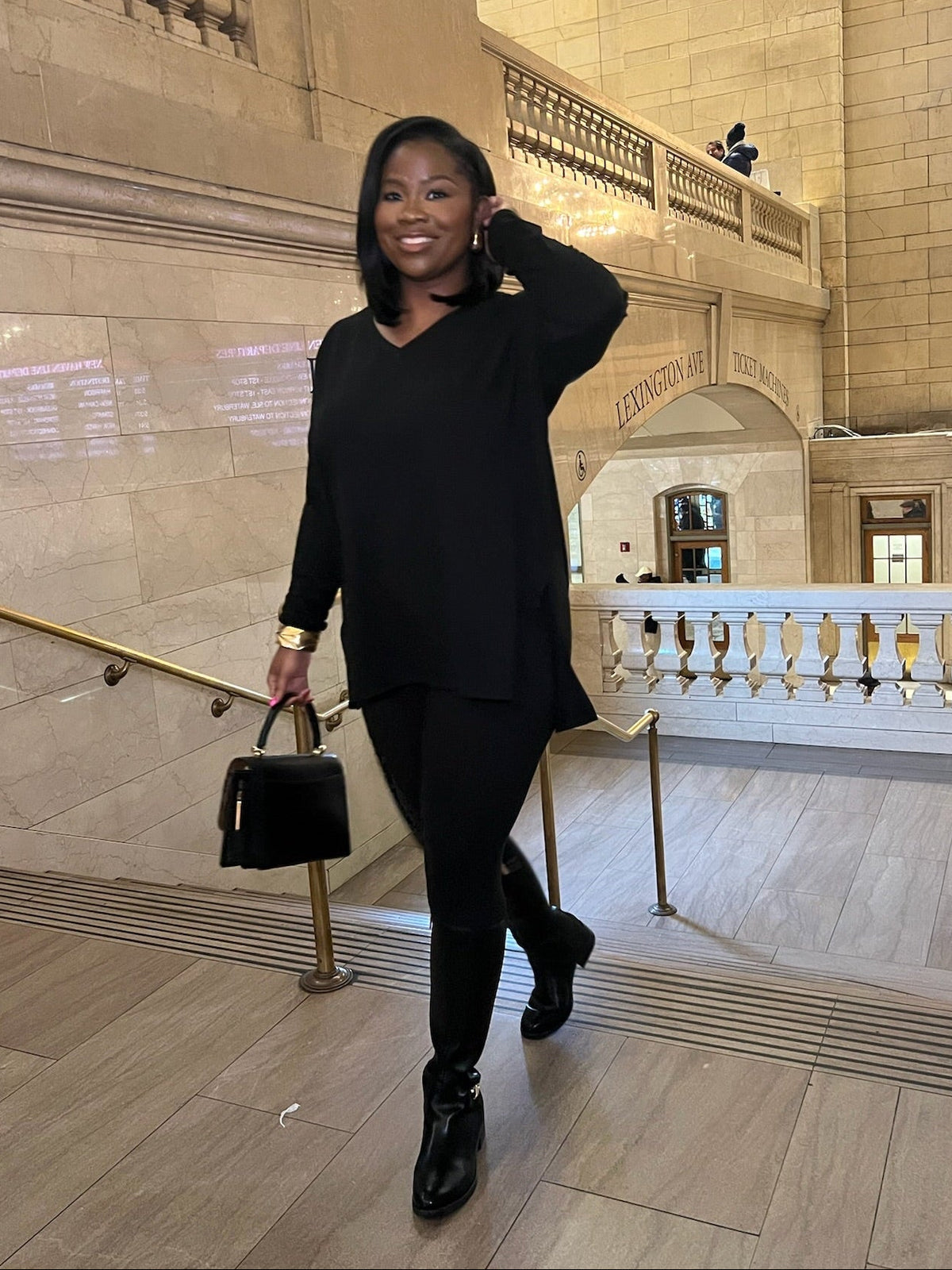 Woman in a black long sleeve matching set posing in a grand hall with marble walls and wooden floors.