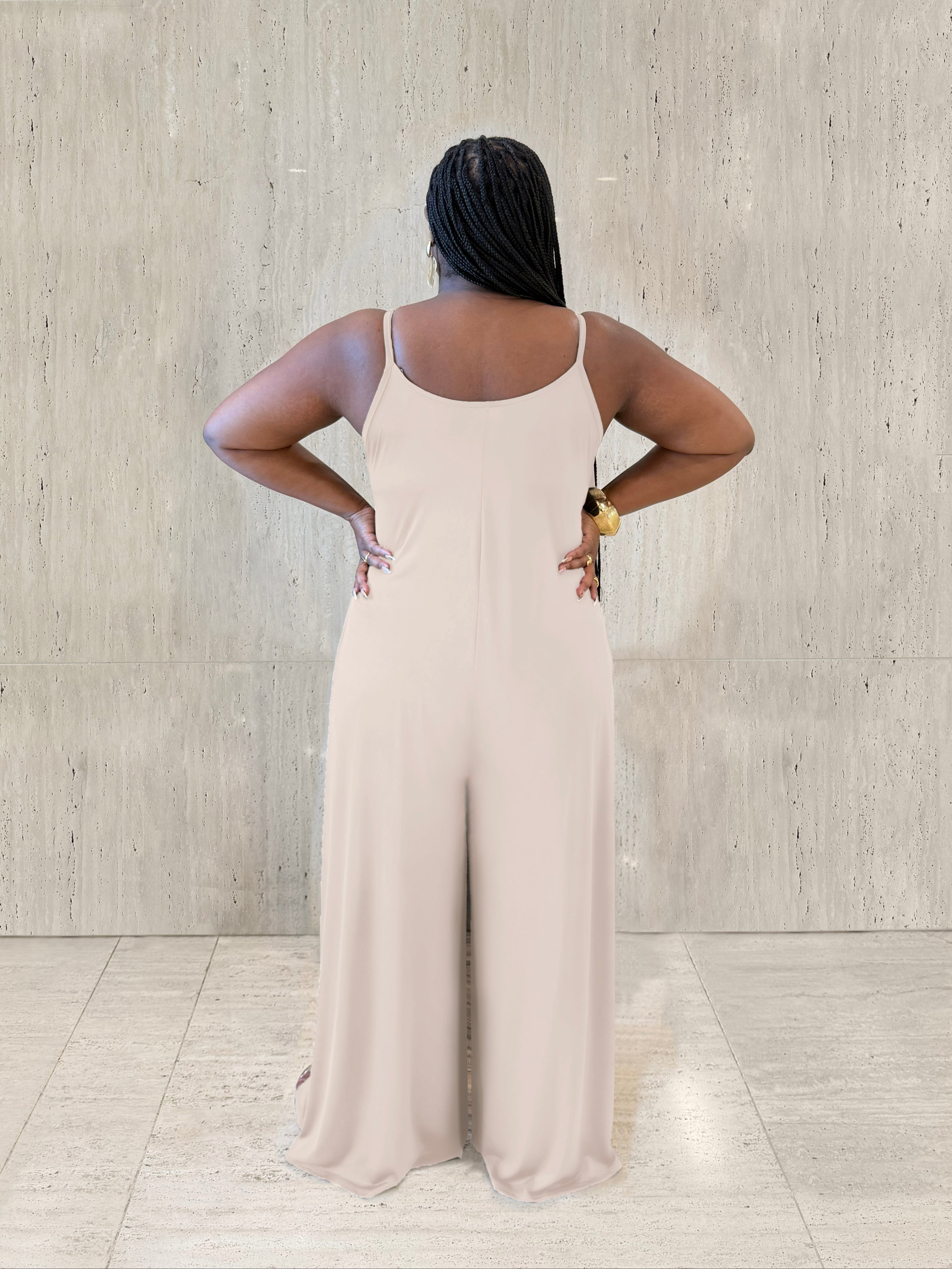 Woman wearing a beige jumpsuit standing against a light gray wall.