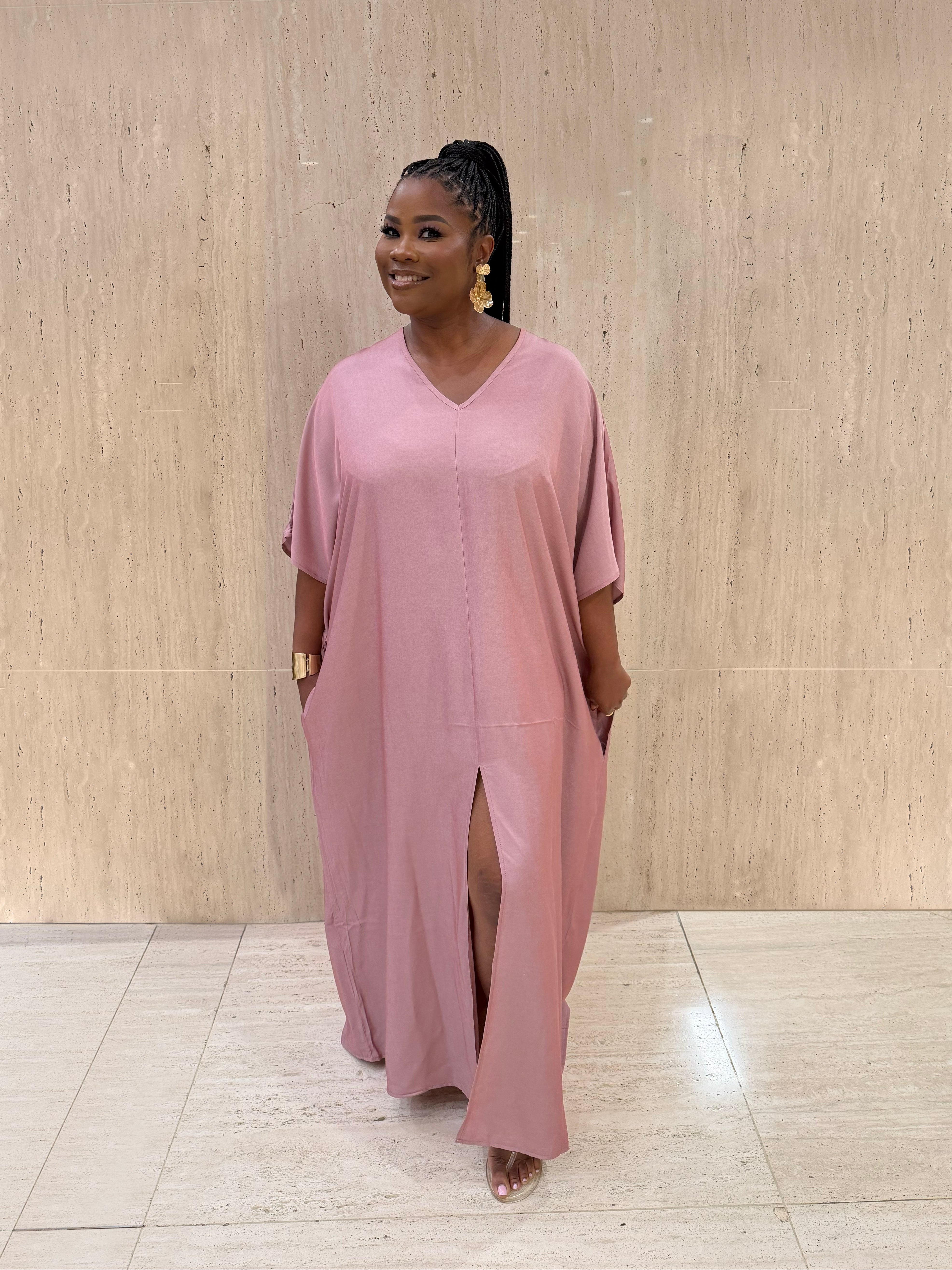 Woman wearing a pink dress standing against a light wooden paneled wall.
