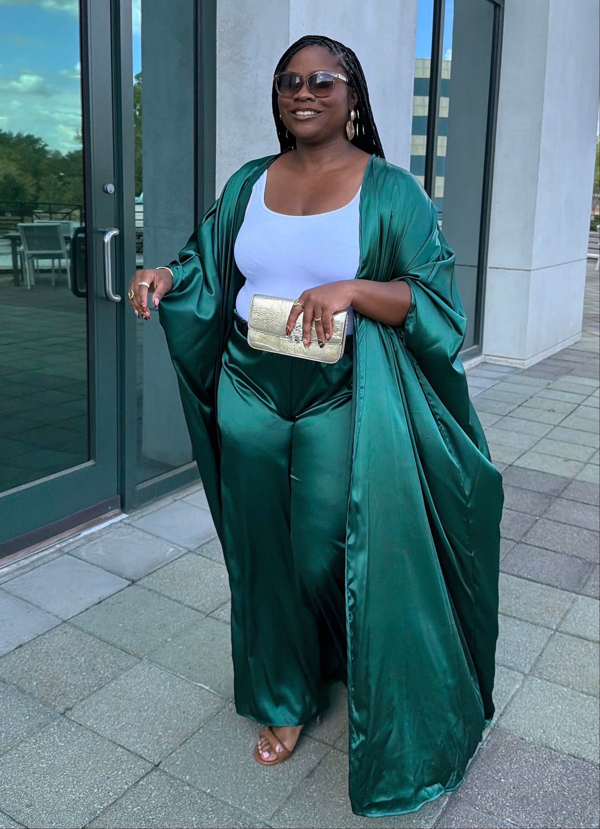 Woman in a green satin outfit standing outside a building with glass doors.