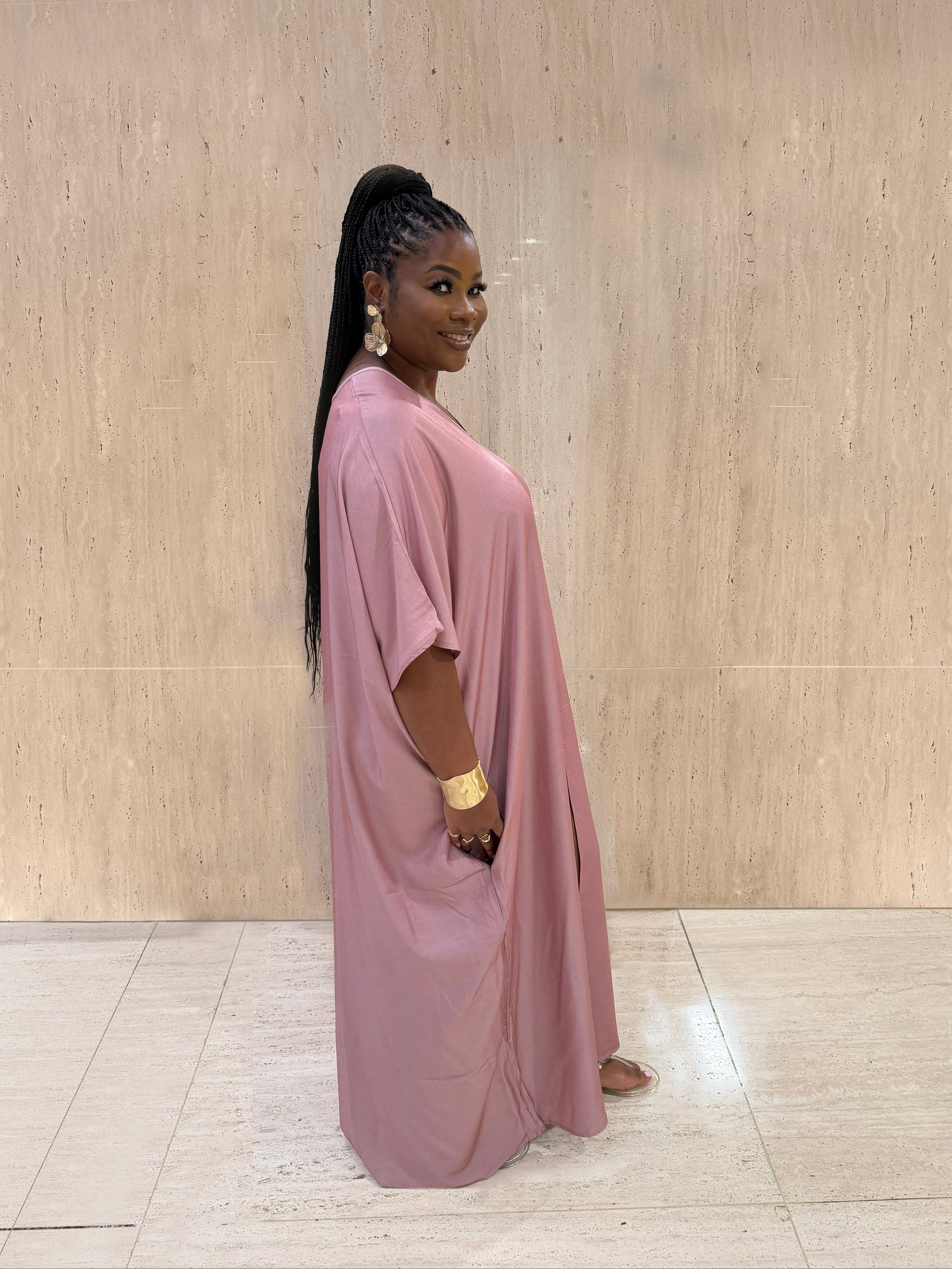 Woman wearing a pink dress standing against a beige wall.