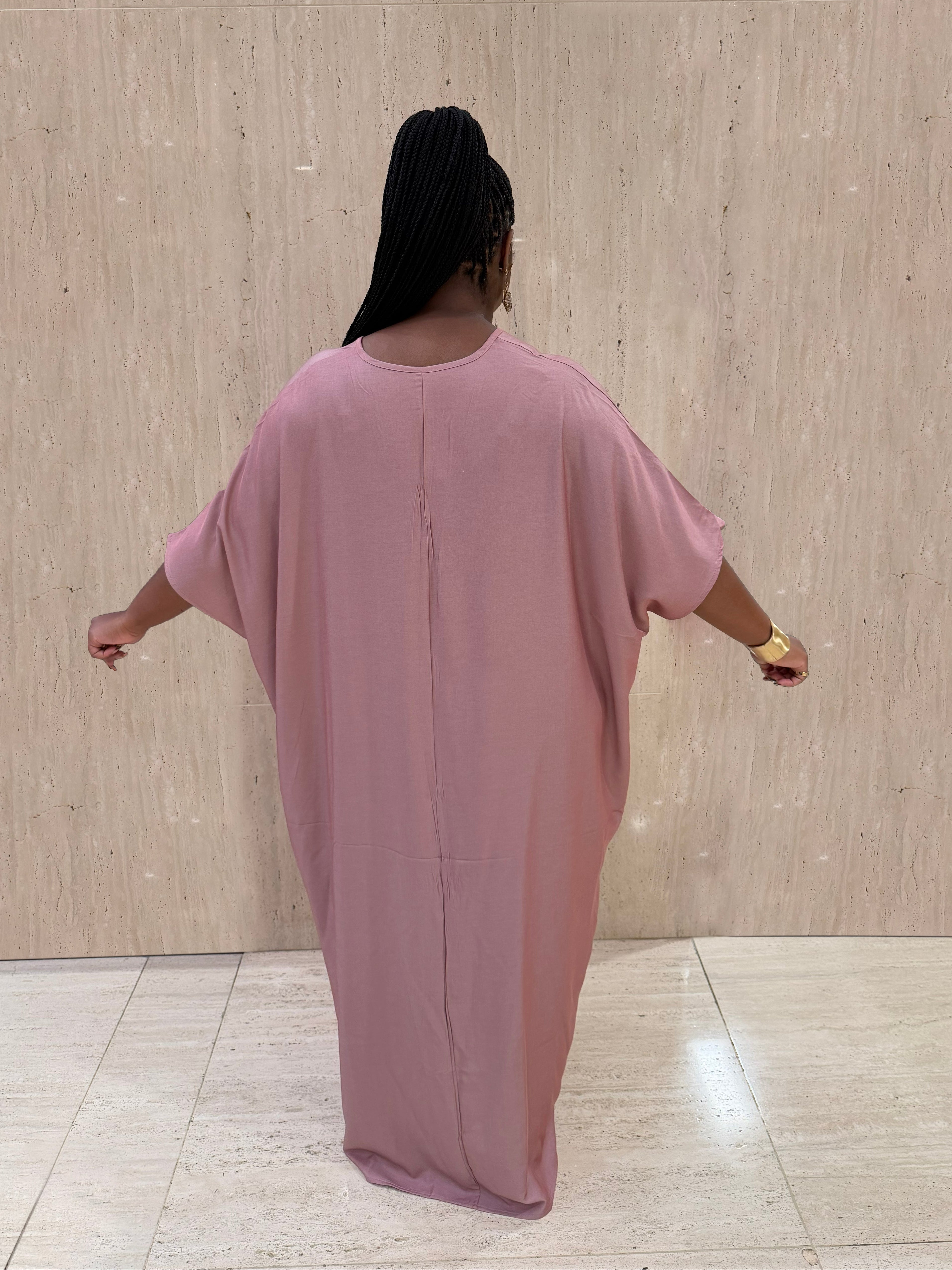 Person wearing a pink dress standing against a beige wall.