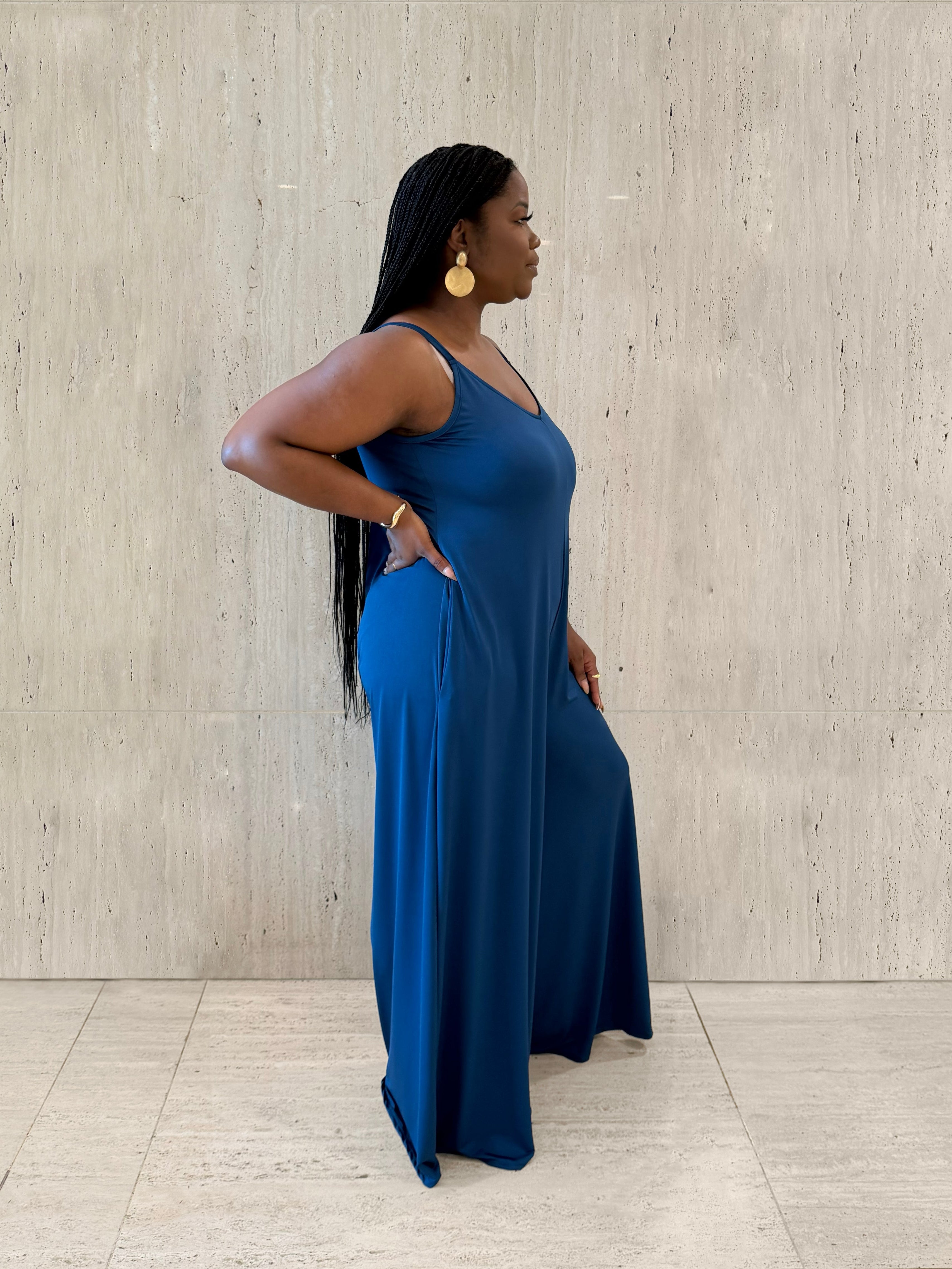 Woman in a blue jumpsuit standing against a light gray wall.