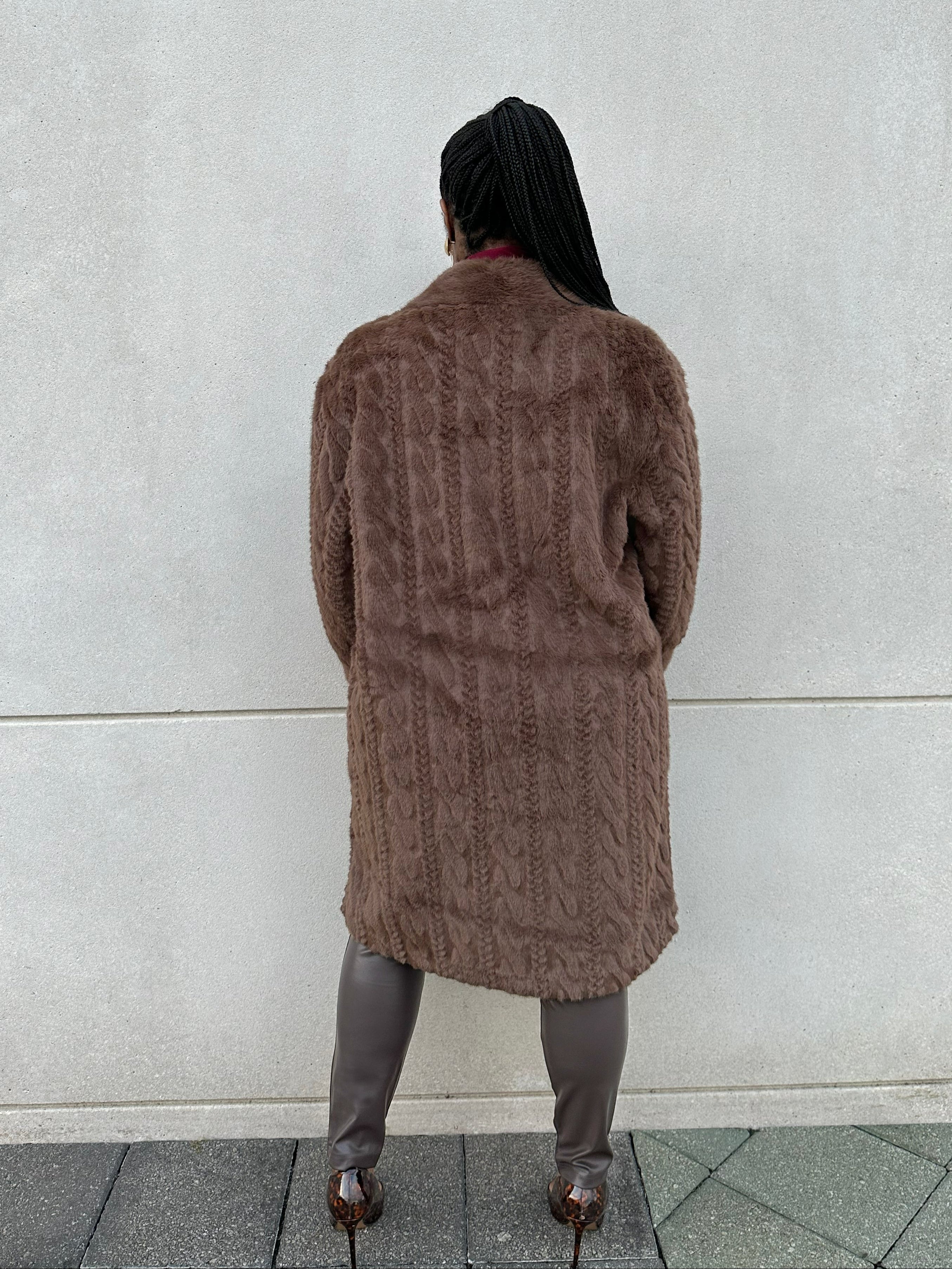 Person wearing a brown textured coat standing against a light gray wall.