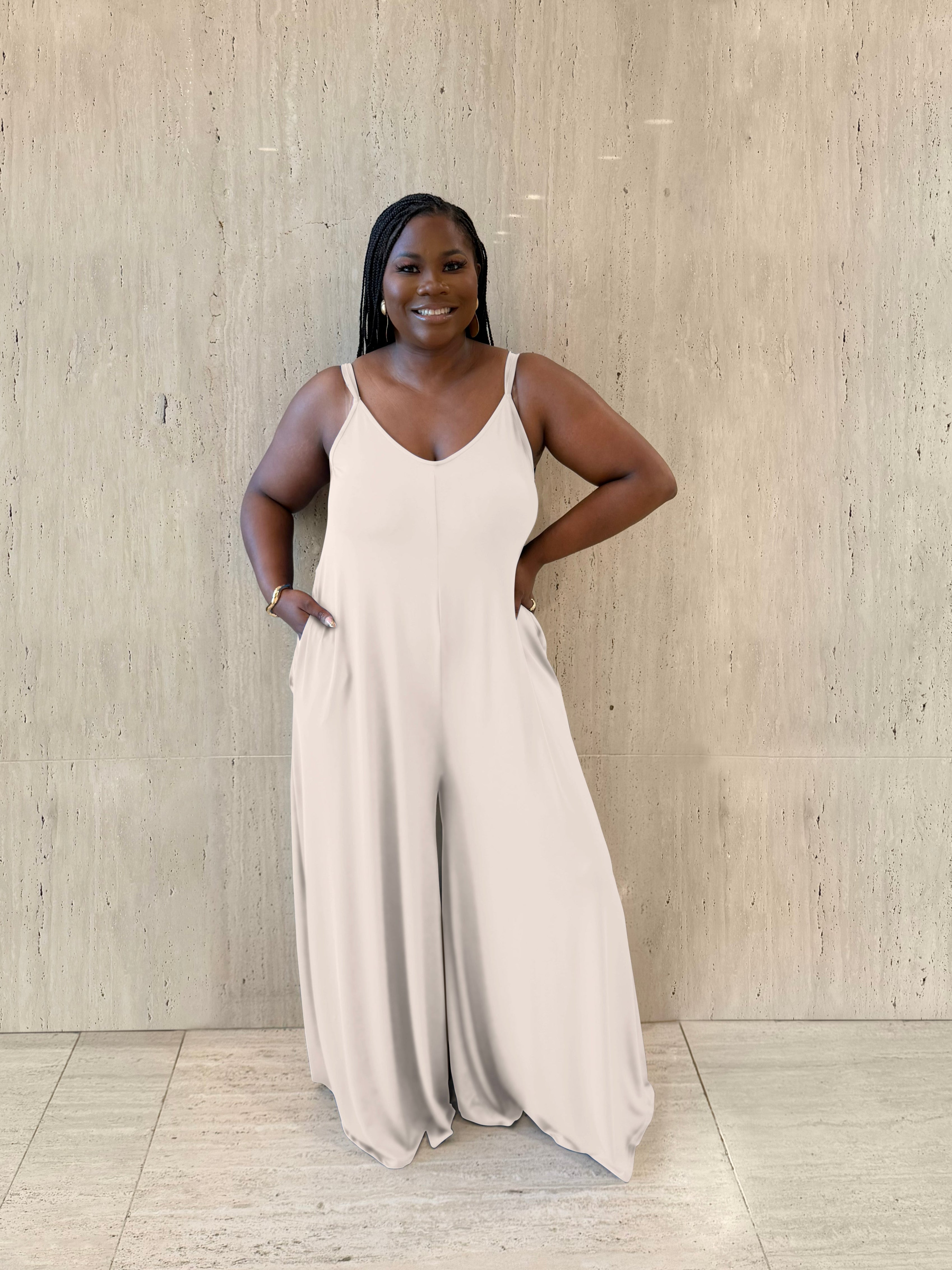 Woman wearing a beige jumpsuit standing against a wooden paneled wall.